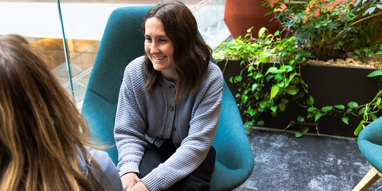 Kristin Good - staff chaplain at UCHealth University of Colorado Hospital, sits in a chair, looking away from the camera, in the Anschutz Health Sciences Building. 