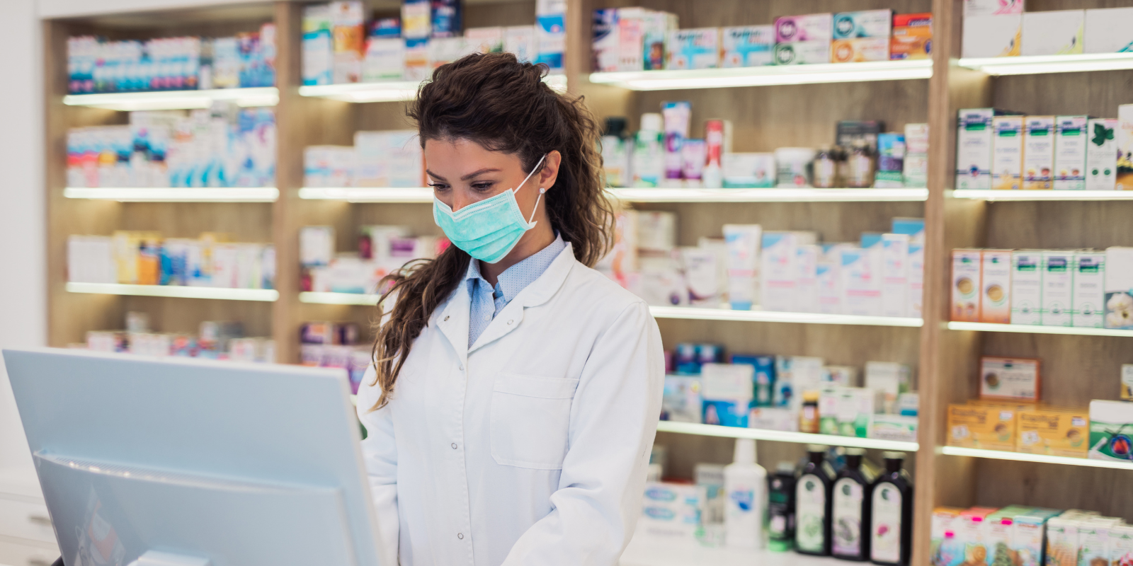 A pharmacist working at a computer wearing a face mast. 